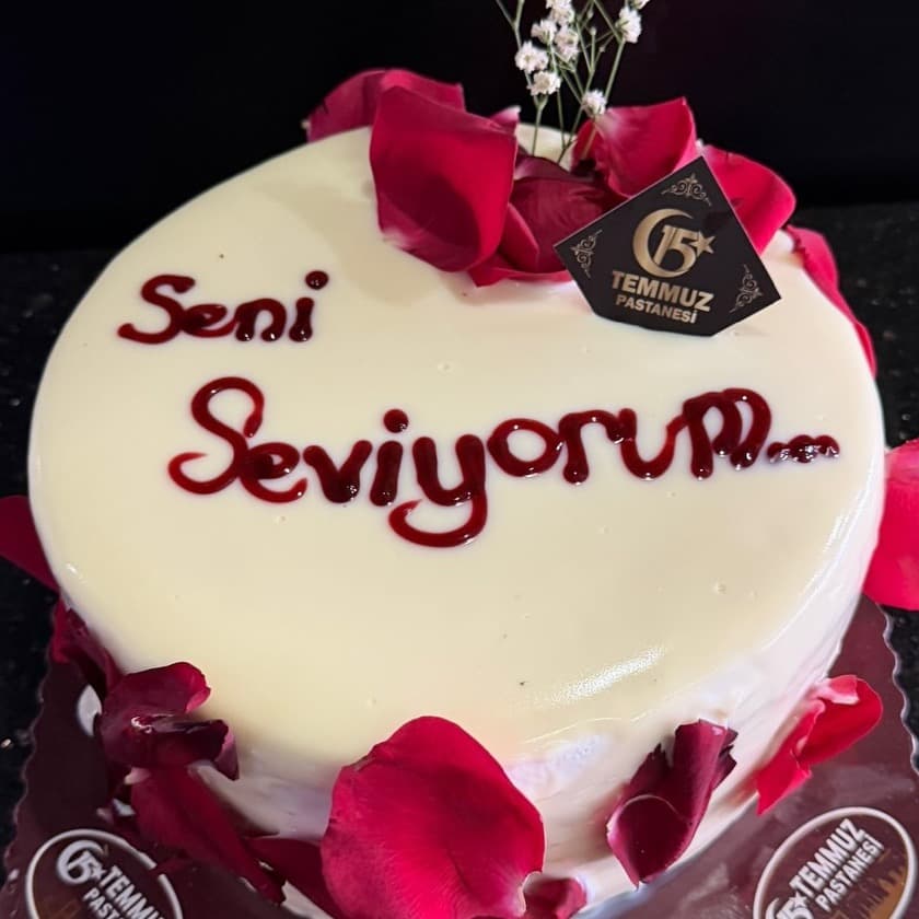 Gül yaprakları arasında kırmızı kremayla 'Seni seviyorum' yazılmış beyaz pasta